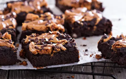 Pyszne brownie z bananami i masłem orzechowym, posypane czekoladowymi kropelkami, kuszą na czarnej kratce.