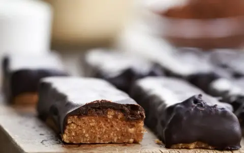 Domowe batony proteinowe przepis: czekoladowe przekąski z widocznym, chrupiącym wnętrzem na drewnianej desce.