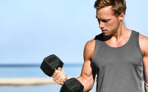Mężczyzna ćwiczy biceps na plaży, wykonując kolejne powtórzenia z hantlem.