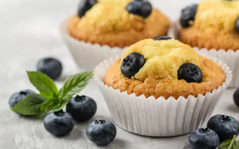 Pyszne muffiny z borówkami, ozdobione świeżymi owocami i listkiem mięty. Idealne na deser.