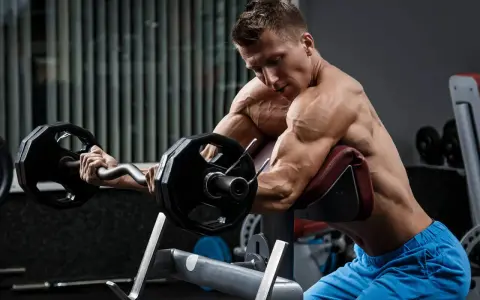 Mężczyzna wykonuje ćwiczenia na biceps i triceps z użyciem sztangi łamanej na modlitewniku.