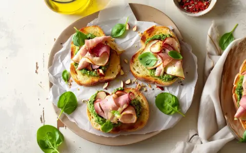 Aromatyczne kanapki z pesto, szynką i świeżą bazylią, posypane migdałami. Idealne na szybką przekąskę.