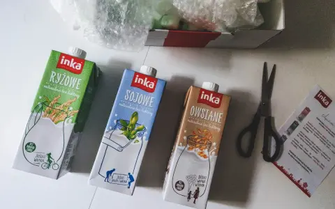 Trzy kartony napojów roślinnych Inka: ryżowy, sojowy i owsiany. Obok nożyczki i ulotka. Tak powstaje mleko owsiane.