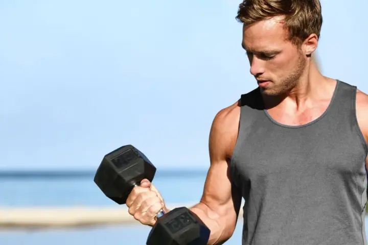 Mężczyzna ćwiczy biceps na plaży, wykonując kolejne powtórzenia z hantlem.