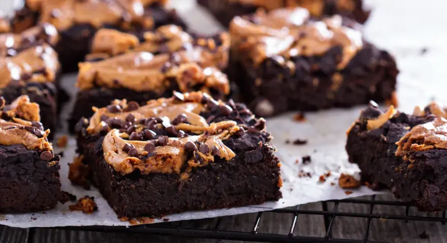 Pyszne brownie z bananami i masłem orzechowym, posypane czekoladowymi kropelkami, kuszą na czarnej kratce.
