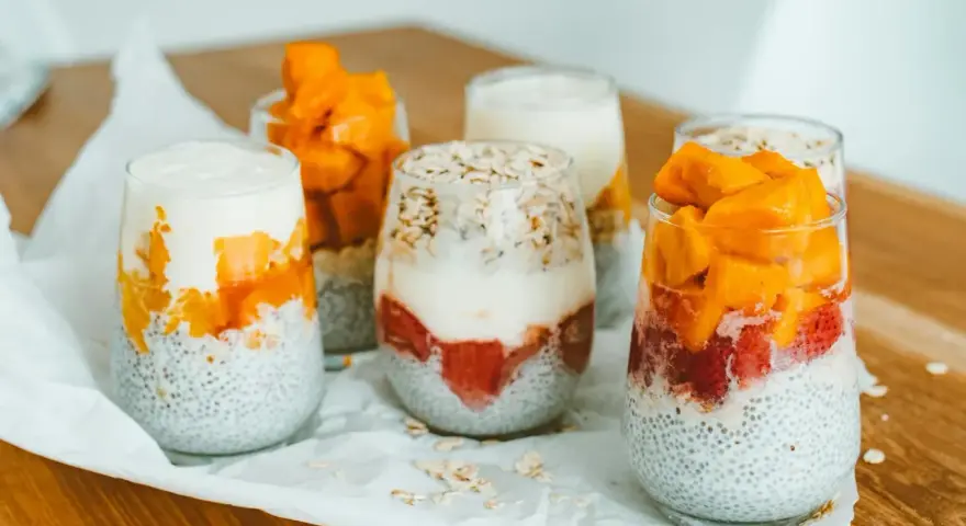 Pyszny deser chia z mango i truskawkami w szklankach, ułożony warstwowo z jogurtem i płatkami owsianymi.