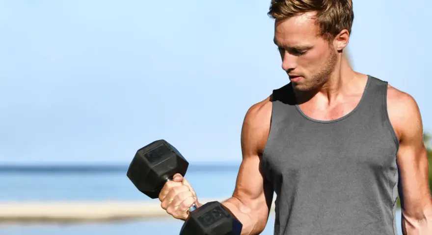 Mężczyzna ćwiczy biceps na plaży, wykonując kolejne powtórzenia z hantlem.