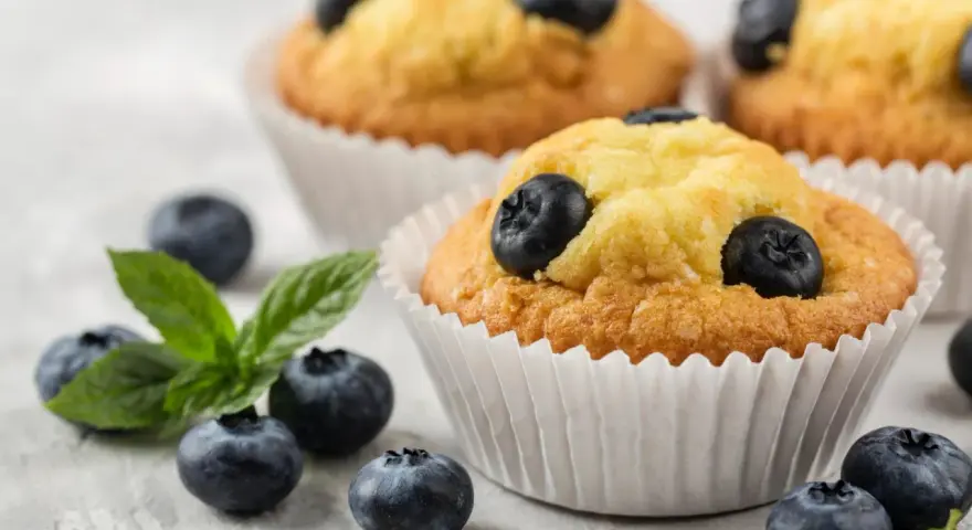 Pyszne muffiny z borówkami, ozdobione świeżymi owocami i listkiem mięty. Idealne na deser.
