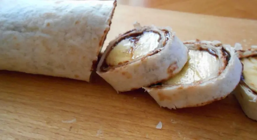 Słodka tortilla z bananem i czekoladą, pokrojona w rolki, wygląda jak pyszny deser.