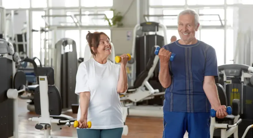 Uśmiechnięta para seniorów ćwiczy z hantlami na siłowni.